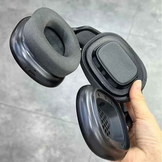 Hand holding a pair of dark grey over-ear headphones with the ear cushions facing up