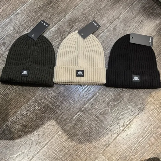 Three ribbed knit beanies in black, cream and dark grey on a wooden surface