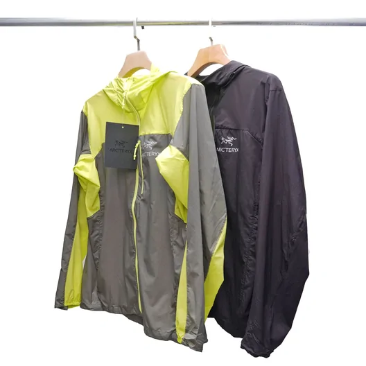 Two light jackets on hangers, one lime and grey, one dark charcoal, against a white wall