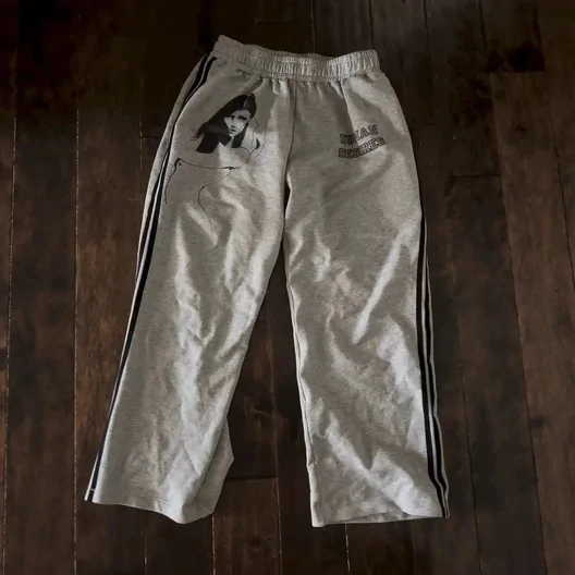 Grey sweatpants with dark side stripes and a small printed photo on one leg, laid on a wooden floor